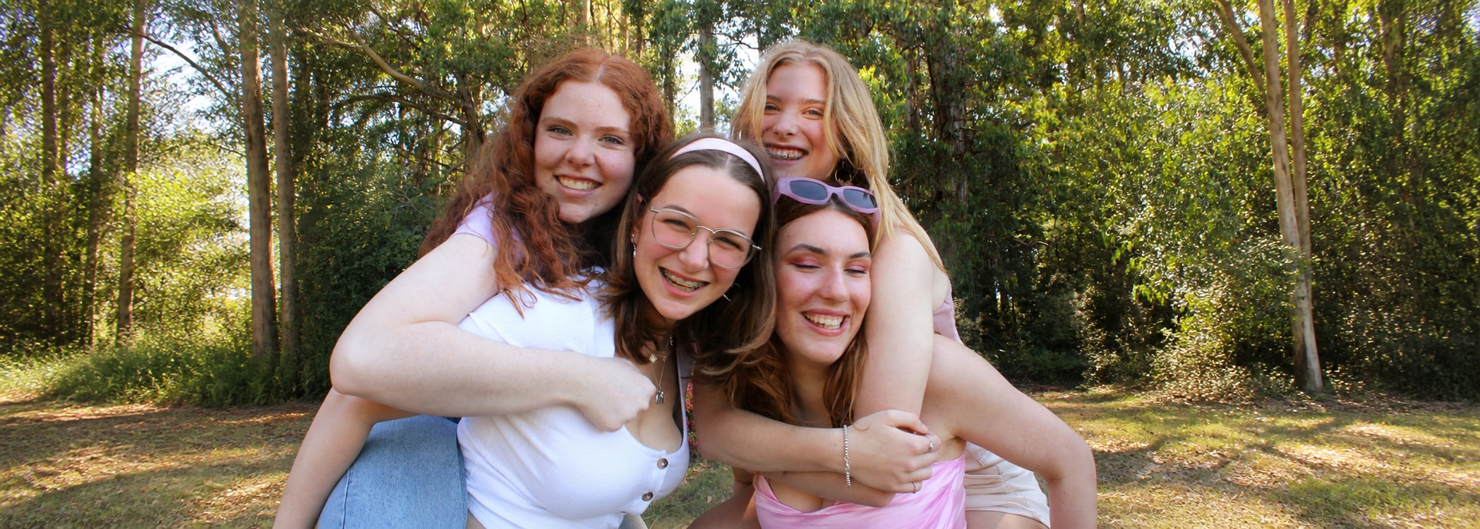Four friends hugging and laughing together in a sunny woodland clearing