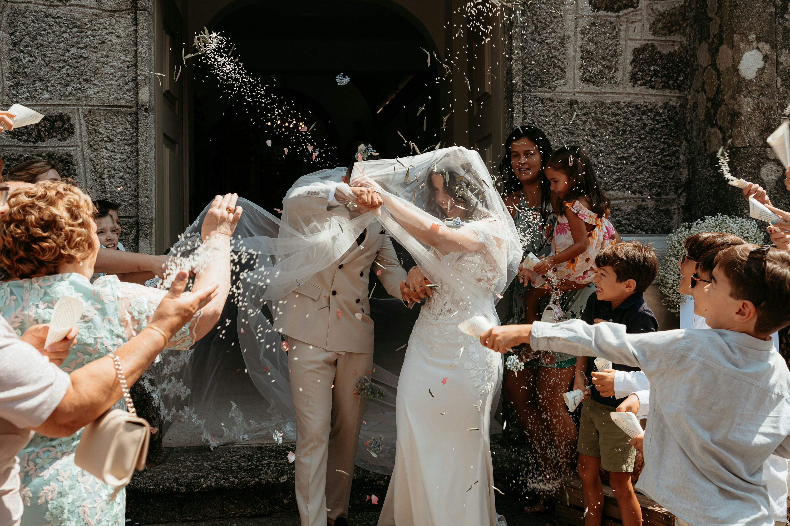 Newlyweds laughing beneath confetti as they leave a church