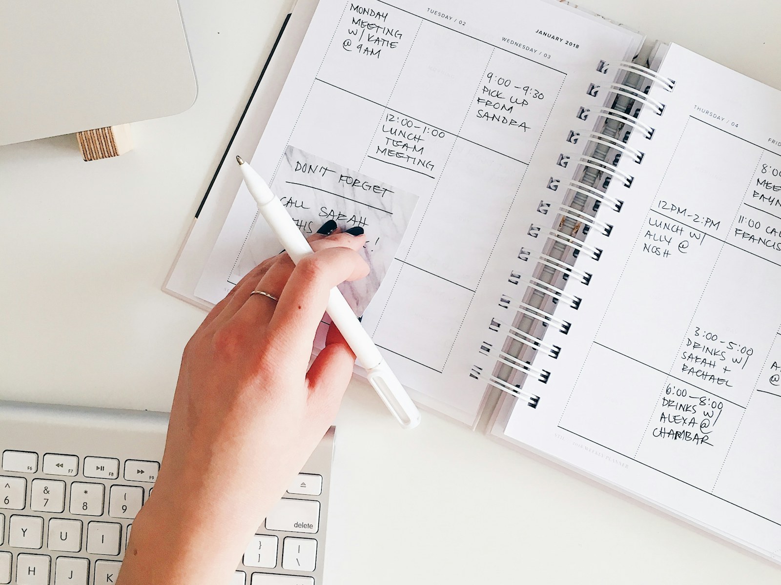 A hand working through a crowded paper planner beside a laptop