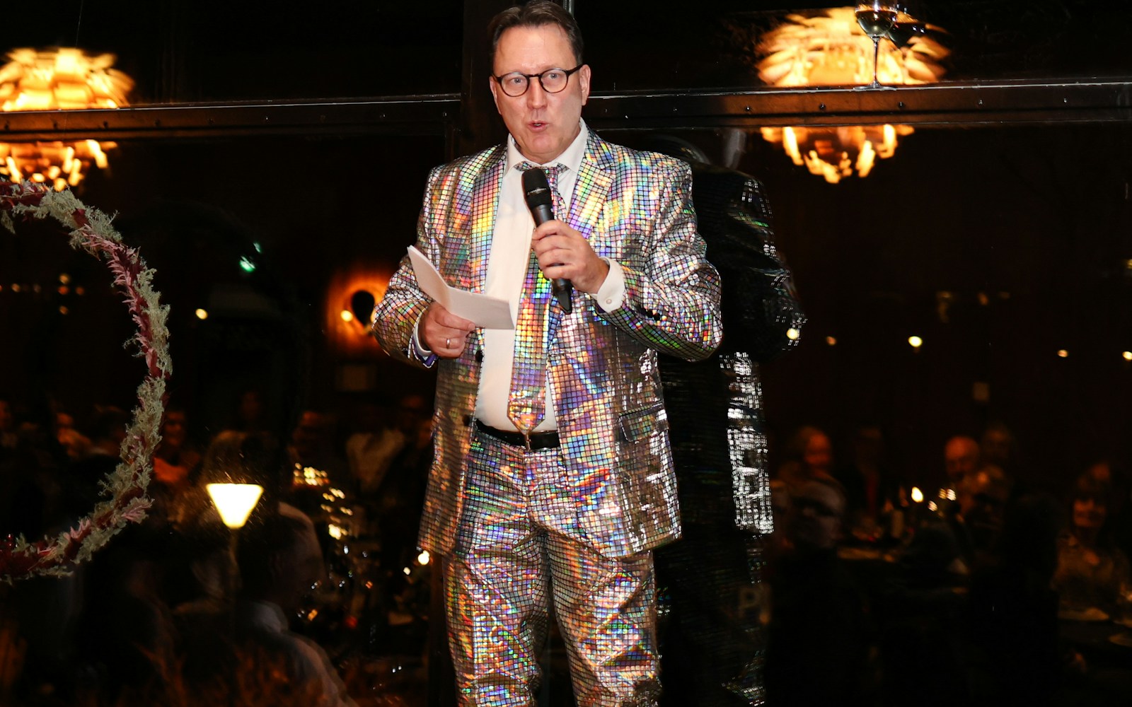 An event host in a sparkling suit speaking into a microphone